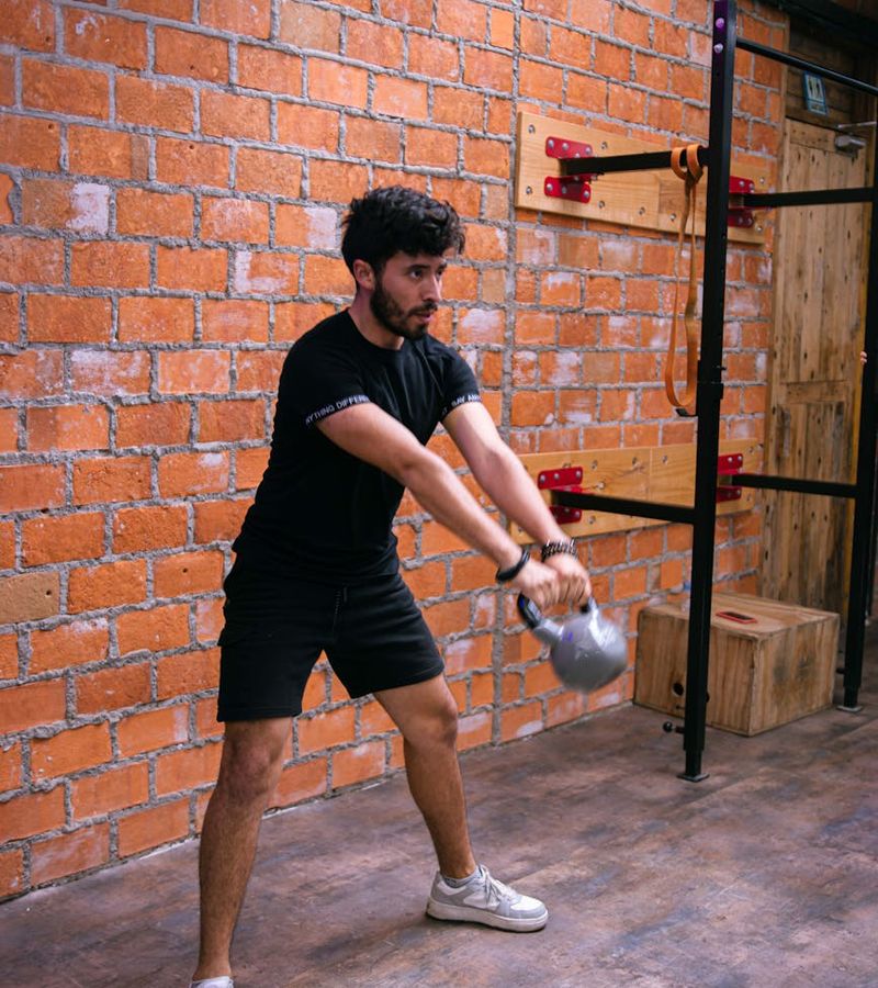 A man focused on his form while lifting a kettlebell in a minimalist setting.